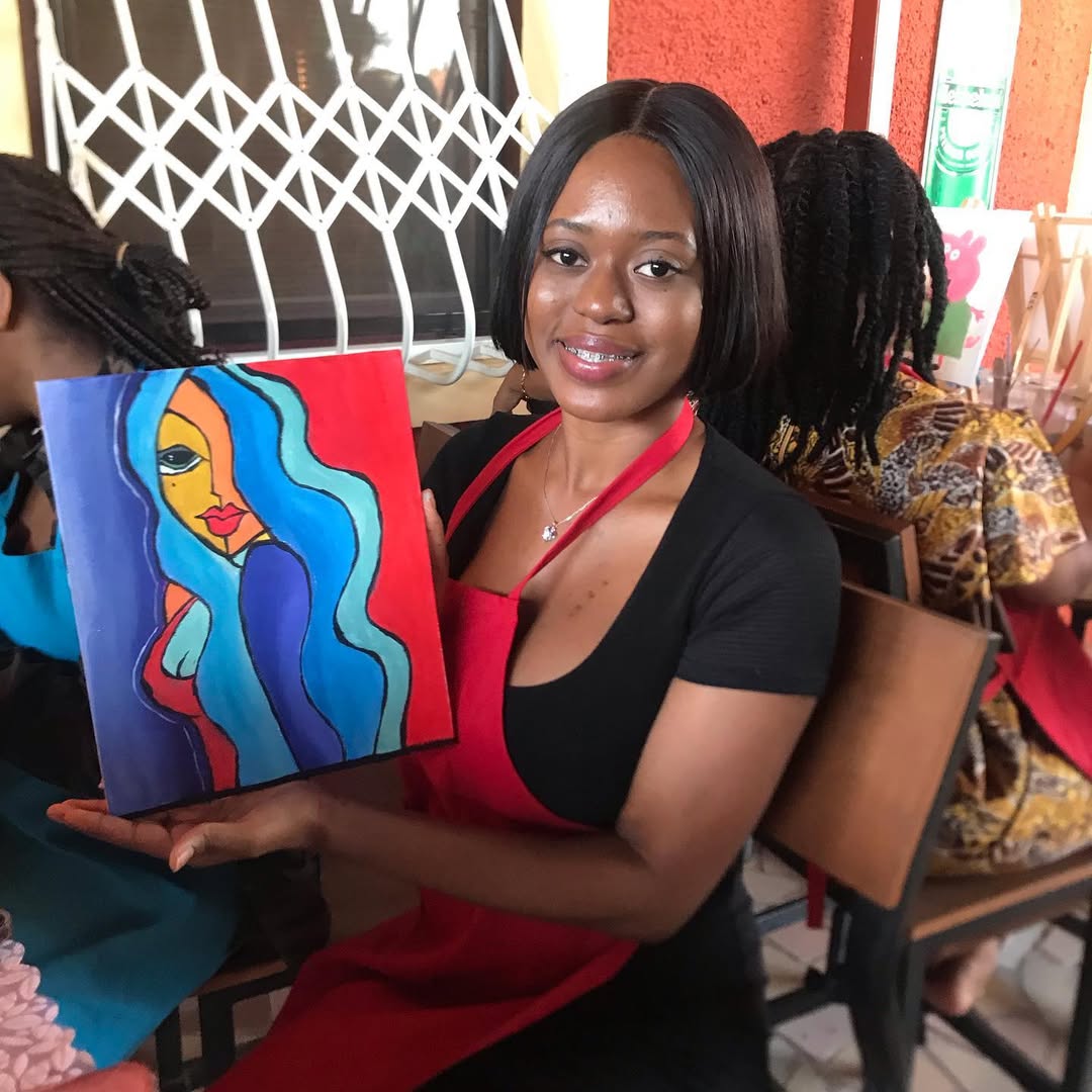 A painter smiling with the bold abstract portrait she painted at a Rhythms Splatters N Sips night