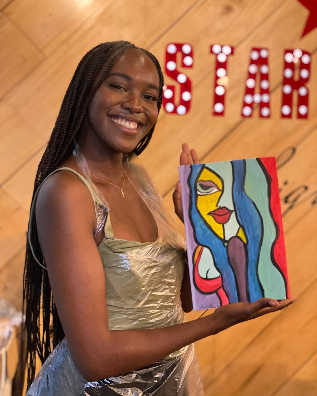 A painter holding a bold cubist-style portrait she painted at a sip & paint night