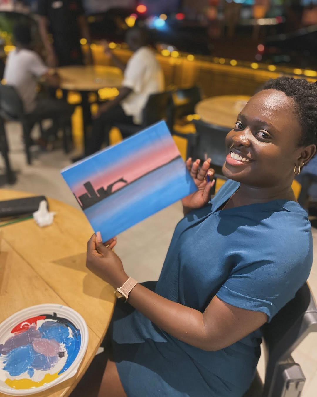 A painter holding a stylised skyline-at-dusk canvas in a lounge